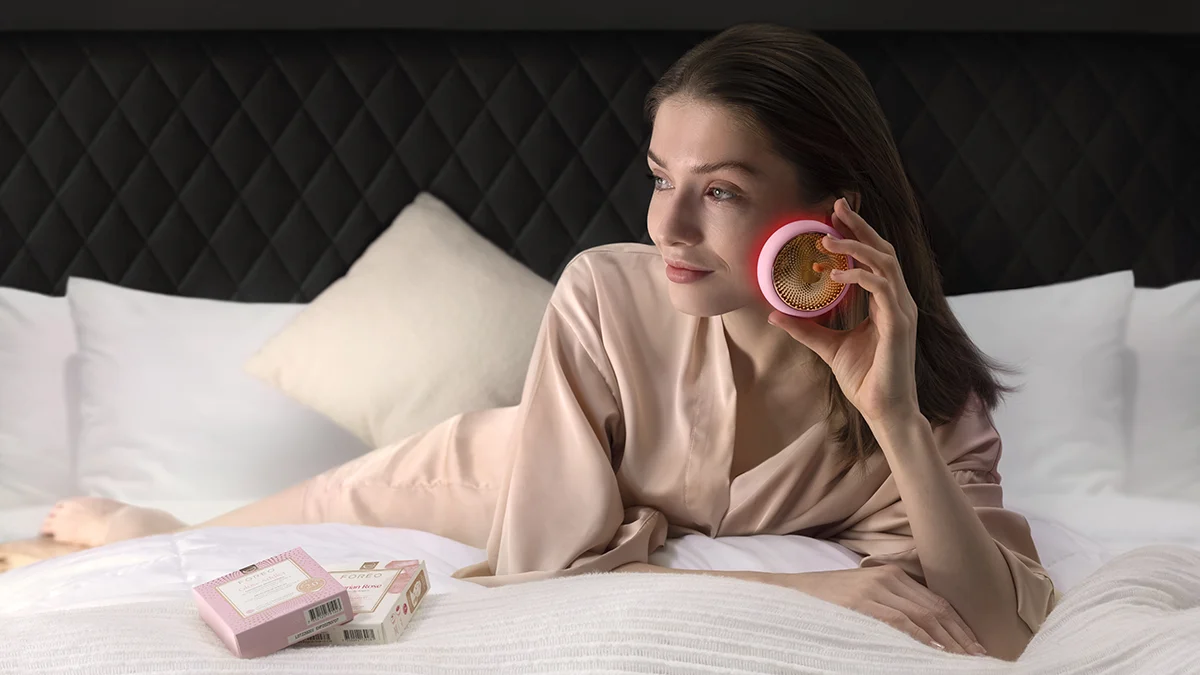 Young woman lying on a bed, using red light therapy at home device